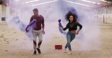 Kafkas erkek ve kadın ırk dansçılarının boş bir depoda, ellerinde sis bombaları dans ve zıplama ağır çekimde antrenman yapmaları ön planda.