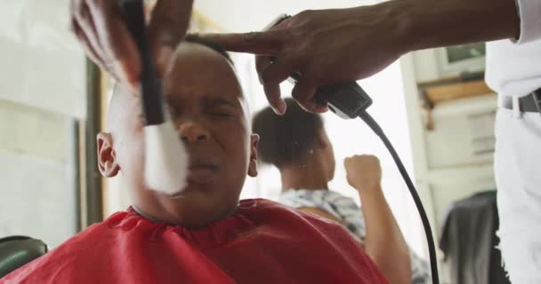 一位非洲男孩在镇上的一家美发店里 在一位非洲男性理发师给他理发后 他的脸被洗净了 他的妈妈在后面等着 动作缓慢 — 图库视频影像