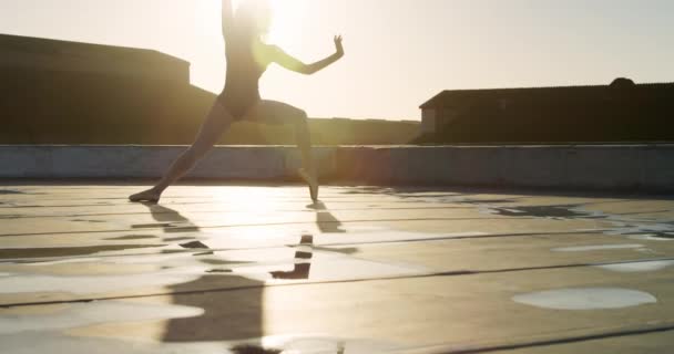 日の出 ストレッチ 背景の建物 スローモーションで屋上で練習混合レースの女性バレエダンサーの側面図 — ストック動画