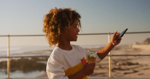 青い空と晴れた日に海辺で時間を楽しむ混合レース少年のサイドビュー 自撮りを取ります アイスクリームを食べます スローモーション — ストック動画