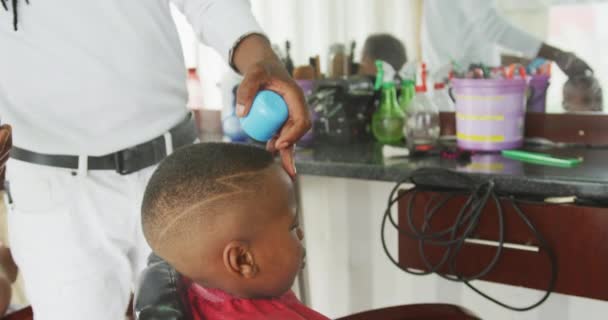 一个非洲男孩在镇上的美发厅里 一个非洲男性理发师用喷雾剂喷他的头发 动作缓慢 — 图库视频影像