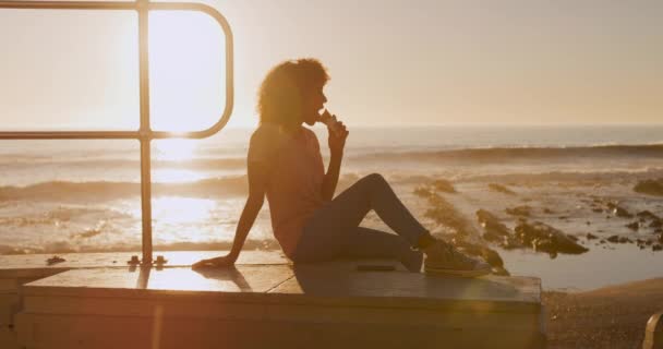 日没の晴れた日に海辺で時間を楽しむ混合レースの女性のサイドビュー アイスクリームを食べます スローモーション — ストック動画