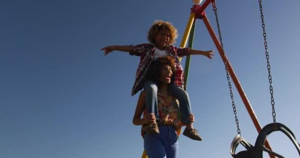 青い空と晴れた日に一緒に遊び場で家族の時間を楽しんで 彼女の肩に彼を運ぶ スローモーション — ストック動画