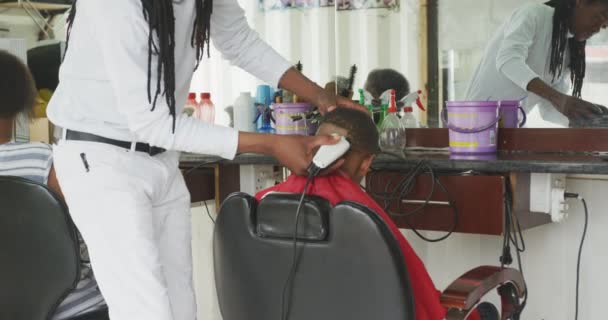 Kasabanın Kuaföründe Rastalı Saçlarıyla Afrikalı Bir Çocuğun Kafasını Tıraş Eden — Stok video