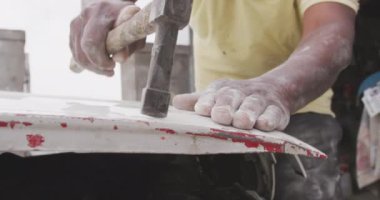 Kasaba atölyesinde bir Afrika panel çırpıcısının ön görüntüsü. Bir arabayı tamir etmek için çekiç kullanıyor. Yavaş çekim.