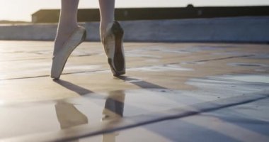 Güneş doğarken çatıda dans eden, parmak uçlarında yürüyen ve zıplayan, arka planda binalar olan kadın balerin bacaklarını kapatın.