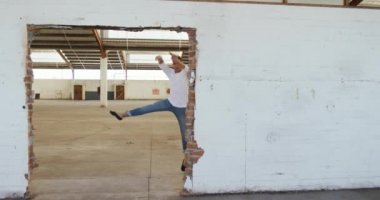 Boş bir depoda dans eden, sıkıntılı bir kapıdan atlayan, ağır çekimde dans eden beyaz bir erkek balerin ön görüntüsü.