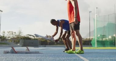 Bir spor stadyumunda antrenman yapan beyaz ve karışık ırktan erkek sporcuların yan görüntüsü, yarış için koşu blokları hazırlıyorlar, yavaş çekim.