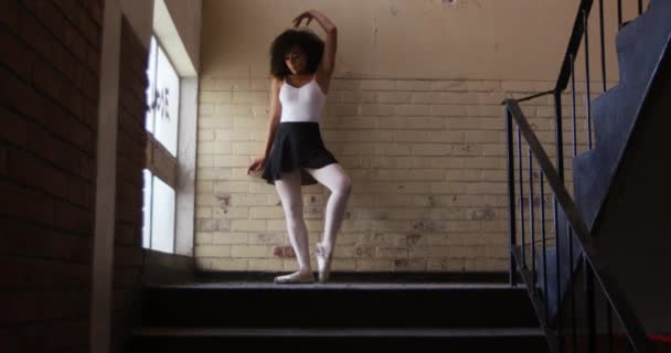 空の倉庫で練習している混合レースの女性バレエダンサーの低角度フロントビュー ダンスや階段でレンガの壁にもたれ スローモーション — ストック動画
