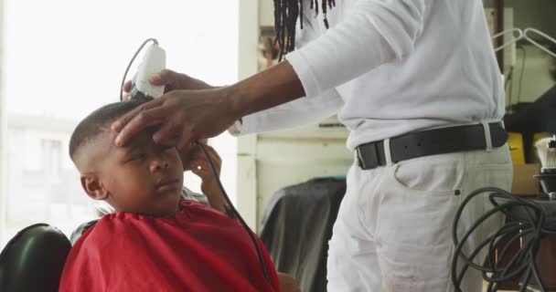 サイドビューアフリカの男性の美容師の真ん中のセクションでは 町のヘアサロンでドレッドロック 剃毛頭アフリカの男の子 スローモーション — ストック動画