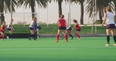 Bir spor stadyumundaki hokey maçı sırasında sahada görev yapan iki beyaz kadın hokey takımının yan görüntüsü, yavaş çekim.