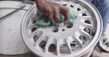 Kasaba atölyesinde kıdemli bir Afrikalı erkek panelcinin ön görüntüsü. Alaşımlı tekerleği temizliyor, ağır çekimde. Capetown Güney Afrika 'da çekildi.