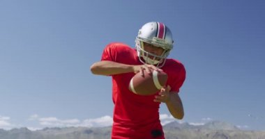 Melez bir Amerikan futbolcusunun bir spor sahasında ağır çekimde topu tutuşu ön planda. Stadyumda Koşu ve Spor Eğitimi.