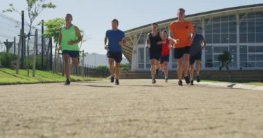 Bir spor sahasında birlikte koşan çok ırklı bir erkek koşucu grubunun düşük açılı ön görüntüsü. Stadyumda ağır çekimde Koşu ve Spor Eğitimi
