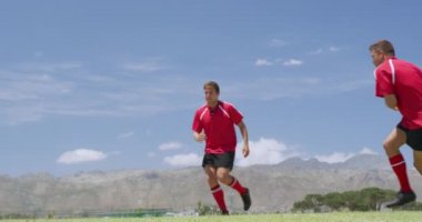 İki rakip takımdan bir grup beyaz erkek rugby oyuncusunun yan görüntüsü. Takım elbiseleri giyiyorlar, sahada oynuyorlar, pas atıyorlar ve ağır çekimde yakalanıyorlar.