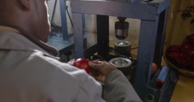 Bir fabrikada çalışan, kriket topu üreten, kriket topunun deri kapağını şekillendiren bir makineyi çalıştıran, Afrika kökenli Amerikalı bir adamın omuz hizasında.