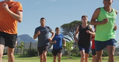 Spor sahasında birlikte çim pistinde koşan çok ırklı bir erkek koşucu grubunun ön görüntüsü.