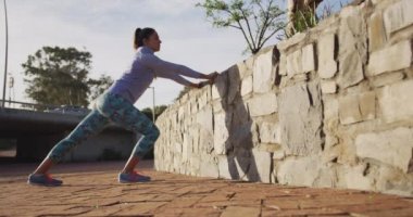 Parkta egzersiz yaparken duvar kenarına uzanan spor kıyafetleri giyen beyaz bir kadının ön görüntüsü, yavaş çekim.