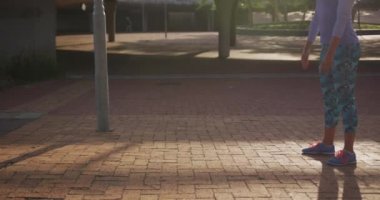 Spor kıyafetleri giymiş genç bir beyaz kadının parkta antrenman yaparken ısınması, çömelmesi, ağır çekim...