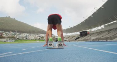 Beyazlı bir erkek sporcunun spor stadyumunda antrenman yaptığını, koşan bloklardan yavaş çekimde koşmaya başladığını. Stadyumda Koşu ve Spor Eğitimi.