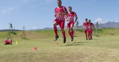 Beyaz erkek futbolculardan oluşan bir takımın ön görüntüsü. Takım elbiseli, güneşin altındaki bir spor sahasında antrenman yapan, bacaklarını yavaş çekimde kaldıran. Stadyumda Koşu ve Spor Eğitimi.