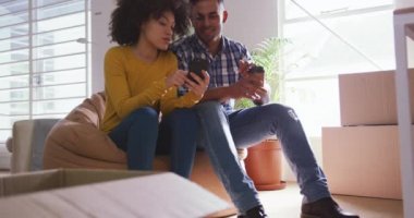 Front view of a mixed race woman and man working in a creative office, talking and sitting next to cardboard boxes, using a smartphone, slow motion
