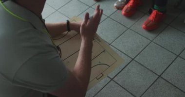 Kafkas erkek hokey koçunun beyaz genç bayan hokey oyuncularıyla konuşması ve hokey maçından önce soyunma odasında bir oyun planı çizmesi.