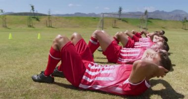 Beyaz erkek futbolculardan oluşan bir takımın yan görüntüsü, takım elbiseli, güneşin altında spor salonunda antrenman yapan, arka arkaya ağır çekimde mekik çeken. Stadyumda Koşu ve Spor Eğitimi.