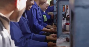 Bir fabrikada çalışan, kriket topları yapan, makine çalıştıran, dönen, gülümseyen ve iş arkadaşlarıyla konuşan Afrikalı Amerikalı bir adamın yan görüntüsü.