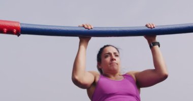 Ön cephede, spor kıyafetleri giymiş, gezinti sırasında barfiks çeken, yavaş çekim yapan beyaz bir kadın görülüyor.