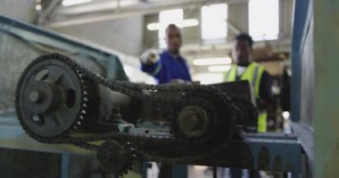 Fabrikada cırcır böceği topları yapan, fabrika atölyesinde tartışan, biri yüksek görüş açısına sahip bir yelek giyen ve elinde bir not panosu olan iki Afro-Amerikan adamın ön görüntüsü.