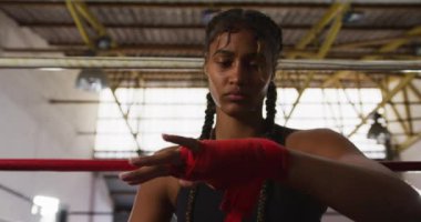 Karışık ırk boksörü, uzun, süslü saçlı, boks salonunda boks ringinde oturan ve ellerini yavaşça saran bir kadın boksör.