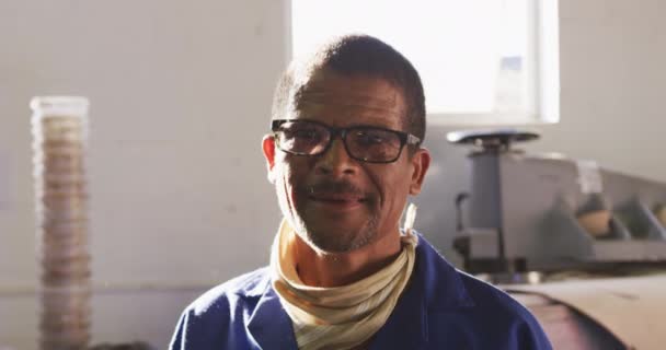 一个非洲裔美国人的画像 他戴着眼镜在一家制造板球球的工厂工作 站在他操作的机器前微笑着 慢动作 — 图库视频影像