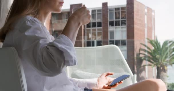 一个白人妇女坐在阳台上喝咖啡 在酒店享受美好时光的侧视图 背景中的建筑物 慢动作 — 图库视频影像