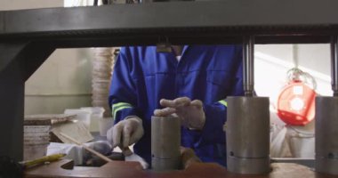 Bir fabrikada çalışan, kriket topları yapan, topların çekirdeği için bir kalıbı ağır çekimde dolduran, eldiven ve tulum giyen bir adamın ön görüntüsü.