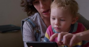 Beyaz bir kadının, evde oturup bebeğiyle vakit geçirmesinin, akıllı telefonuna bakmasının, yavaş çekimde izlemesinin ön görüntüsü.