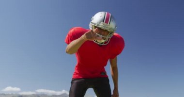 Melez bir Amerikan futbolcusunun, arka planda mavi gökyüzü olan bir spor sahasına yavaşça işaret ettiği bir görüntü. Stadyumda Koşu ve Spor Eğitimi.
