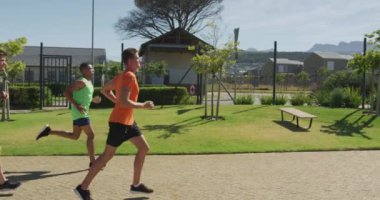 Bir spor sahasında birlikte koşan çok ırklı bir erkek koşucu grubunun yan görüntüsü. Stadyumda ağır çekimde Koşu ve Spor Eğitimi