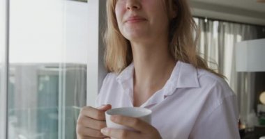 Front view close up of a Caucasian woman enjoying quality time in a hotel, standing in living room drinking coffee. slow motion