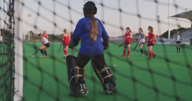 Beyazlı genç bir hokey takımının kalecisinin arka görüntüsü sahada, bir spor stadyumundaki hokey maçında kaleyi savunuyor, yavaş çekim.