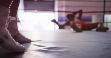 Boks ringinde hareket eden ve zıplayan bir kadın boksörün botlarının yan görünüşü. Rakibi halatların üzerinde yatıyor. Ringin diğer tarafında baygın yatıyor.