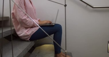 Side view of a Caucasian woman enjoying quality time in a hotel, sitting on the stairs and using laptop, slow motion