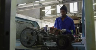 Bir fabrikada çalışan, kriket topları yapan, kriket topunun çekirdeği için doldurulmuş bir kalıbı bir makineye takan, eldiven ve tulum giyen Afrikalı bir Amerikalı 'nın ön görüntüsü.