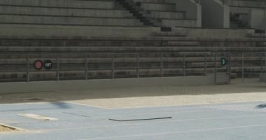 Bir spor stadyumunda antrenman yapan, uzun atlama yapan, yavaş çekim yapan beyaz bir erkek sporcunun yan görüntüsü. Stadyumda Koşu ve Spor Eğitimi.