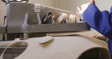 Yan görüntüde, gözlüklü bir Afrikalı Amerikalı fabrikada çalışıyor, kriket topları yapıyor, ayakta duruyor ve deri şekilleri kesen bir makine kullanıyor, yavaş çekim.