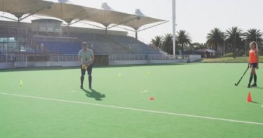 Kafkas erkek hokey koçunun beyaz genç bayan hokey oyuncularına hokey oynamadan önce sahada ısınmaları için talimat vermesi.