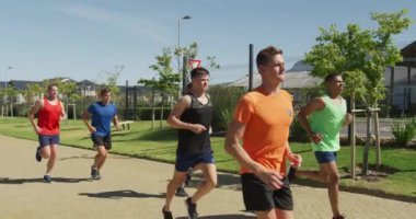 Bir spor sahasında birlikte koşan çok ırklı bir erkek koşucu grubunun yan görüntüsü. Stadyumda ağır çekimde Koşu ve Spor Eğitimi