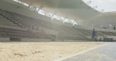 Spor stadyumunda antrenman yapan, uzun atlama yapan, yavaş çekim yapan melez bir erkek sporcunun ön görüntüsü. Stadyumda Koşu ve Spor Eğitimi.