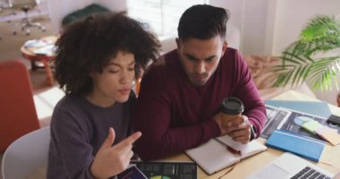 Front view of a mixed race woman and man working in a creative office, discussing, man holding a take away coffee cup, slow motion