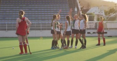 Bir spor stadyumundaki hokey maçında sahada oynayan iki genç beyaz kadın hokey takımının yan görüntüsü. Bir takım elini kaldırıyor ve bir gol, yavaş çekim ve beşlik çakıyor.